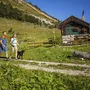 Zwei Menschen wandern mit einem Hund auf einem Pfad nahe einer Hütte im Salzkammergut.