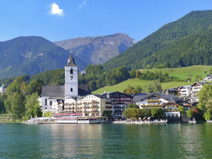 Kirche und Gebäude am Ufer des Wolfgangsees, umgeben von Bergen.