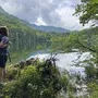 Wanderer steht am Ufer eines Sees im Salzkammergut, umgeben von Wald und Bergen.