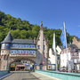 Stadttor im Jugendstil mit Fahnen und bewaldetem Hügel im Hintergrund