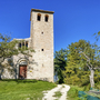 Kirche San Giuliano bei Spoleto, umgeben von Bäumen, klarer blauer Himmel.