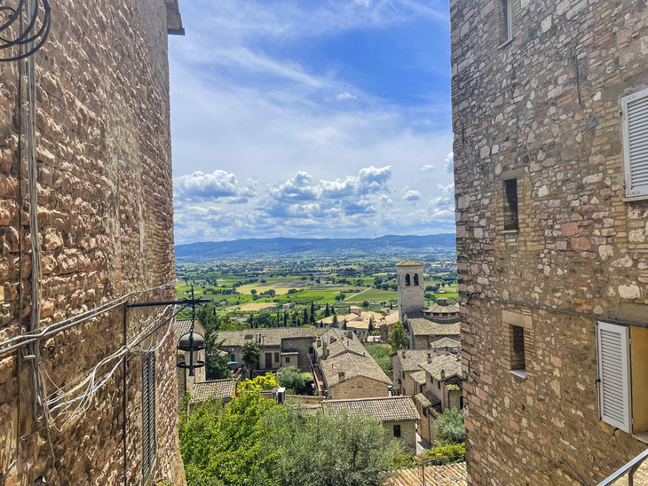 Blick durch enge Gasse auf grünes Tal und Himmel in Umbrien, Italien.