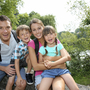 Familie lächelt beim Wandern auf einer Brücke im Grünen.
