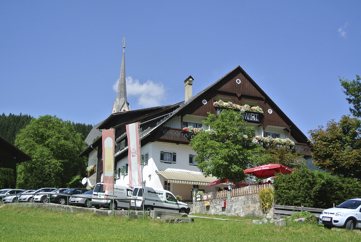 Gasthaus mit Garten und Kirchturm im Hintergrund bei klarem Himmel