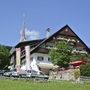 Gasthaus mit Garten und Kirchturm im Hintergrund bei klarem Himmel