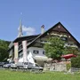 Gasthaus mit Garten und Kirchturm im Hintergrund bei klarem Himmel