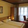 Hotelzimmer mit Doppelbett, Wandschrank, Tisch und Stühlen, Fenster mit Gardinen.