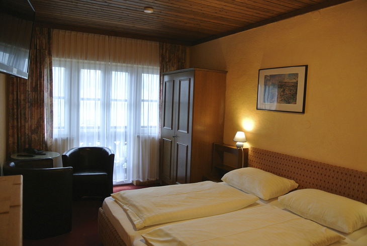 Gemütliches Hotelzimmer mit Doppelbett, Schrank, Sessel und Fenster.