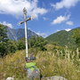 Kreuz auf Wiese mit Bergen und blauem Himmel im Hintergrund