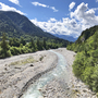 Flussbett mit bewaldeten Bergen und blauem Himmel im Hintergrund