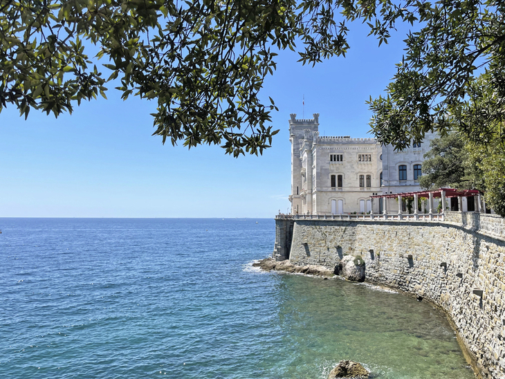 Schloss an der Küste mit Blick auf das Meer und umgeben von grünen Bäumen.