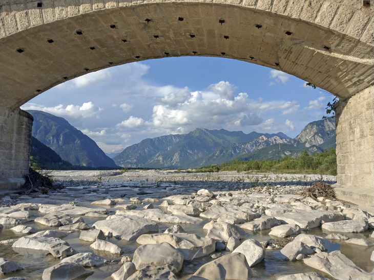 Steinbrücke über Fluss mit Bergkulisse im Hintergrund
