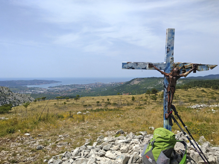 Kreuz und Rucksack mit Blick auf Küstenlandschaft und Meer im Friaul, Italien.