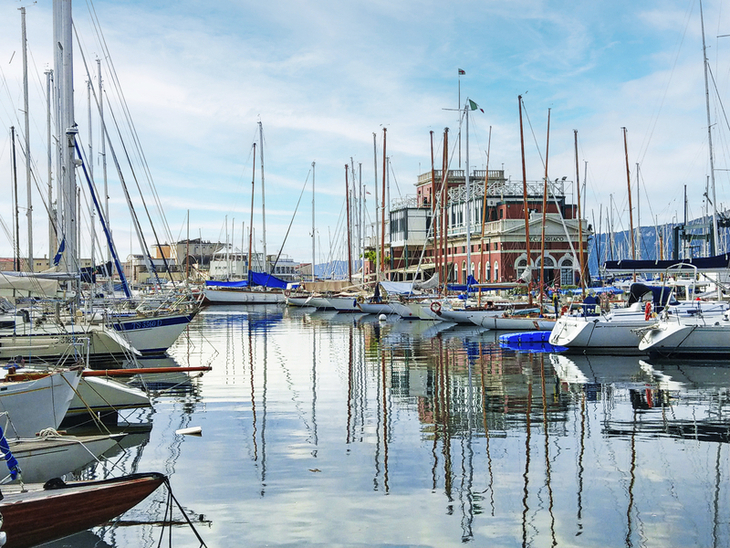Boote liegen im Hafen von Triest vor einem Gebäude.