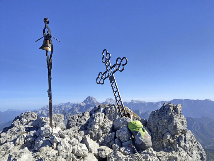 Person mit Rucksack am Gipfelkreuz auf der Cima del Cacciatore in den Julischen Alpen.