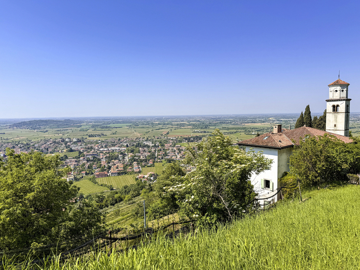 Ausblick auf Landschaft mit Kirche, Bäumen und einem Dorf im Hintergrund unter blauem Himmel.
