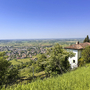 Ausblick auf Landschaft mit Kirche, Bäumen und einem Dorf im Hintergrund unter blauem Himmel.