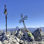Gipfelkreuz auf felsigem Berggipfel mit Rucksack im Vordergrund