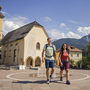 Wanderer auf einem Stadtplatz in Tarvis, Italien, mit Kirche im Hintergrund.