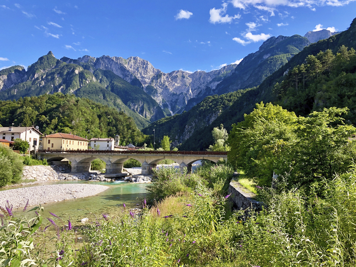 Brücke über Fluss vor Bergpanorama in den Alpen in Friaul, Italien.