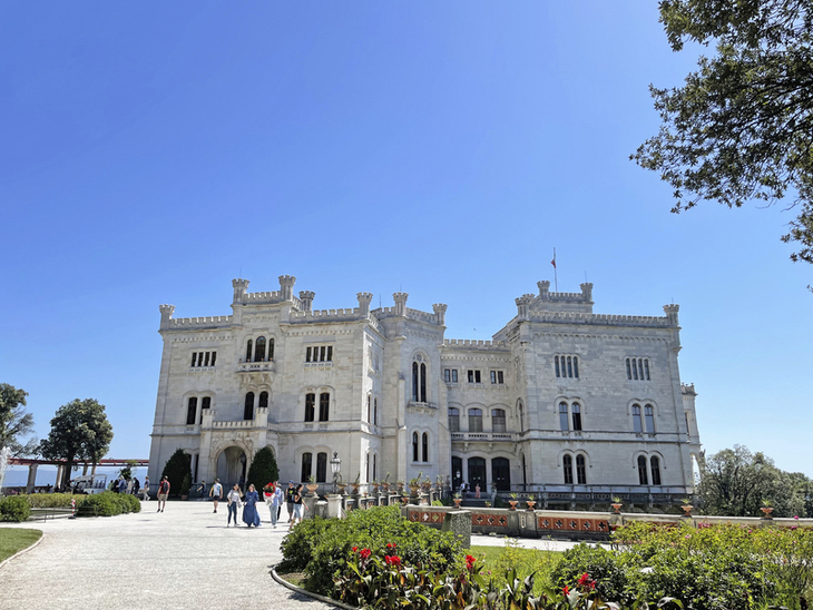 Schloss Miramare im Park bei sonnigem Wetter mit Besuchern im Vordergrund.