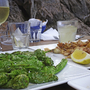Tapas-Gericht auf einem Tisch mit Getränken und Felsen im Hintergrund.
