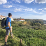 Wanderer blickt auf Küstenlandschaft mit Häusern und Meer im Hintergrund.