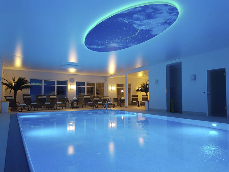 Innenpool im AVALON Bellevue Hotel mit blauer Beleuchtung und Sitzecke im Hintergrund.