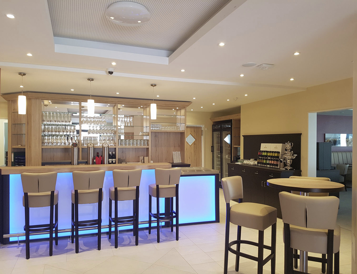 Moderne Hotelbar mit beleuchtetem Tresen und gepolsterten Hockern.