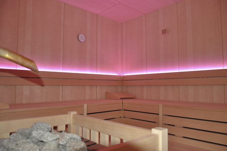 Innenansicht einer Sauna mit Holzbänken und rosa Beleuchtung.