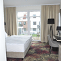 Hotelzimmer mit Bett, Schreibtisch, Balkon und Blick auf andere Gebäude.