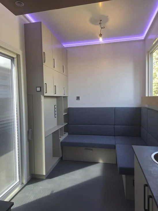 Innenansicht eines modernen Tiny Houses mit Sitzgelegenheiten und violetter Beleuchtung.
