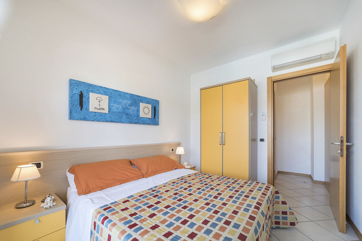 Blick in ein helles Schlafzimmer mit Doppelbett und farbenfroher Bettdecke.