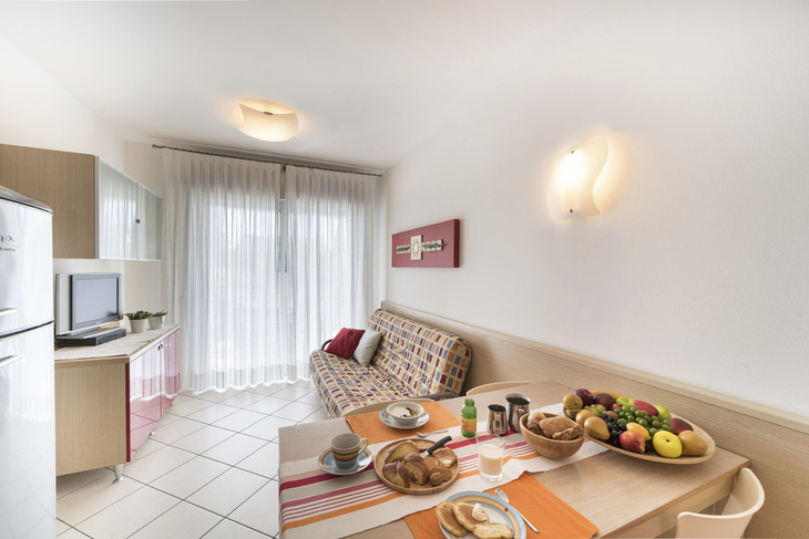 Wohnraum mit Esstisch, Sofa, Fernseher, und großen Fenstervorhängen.