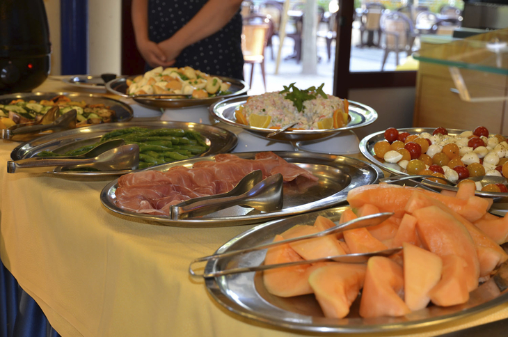 Buffet mit Melone, Schinken, Tomaten-Mozzarella-Salat und anderem Essen auf Silberplatten.