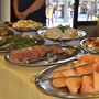 Buffet mit Melone, Schinken, Tomaten-Mozzarella-Salat und anderem Essen auf Silberplatten.