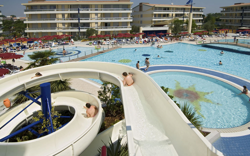 Poollandschaft mit Wasserrutsche und Gebäuden im Villaggio Planetarium Resort in Bibione.