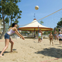 Menschen spielen Beachvolleyball im Sand neben einem Pavillon.