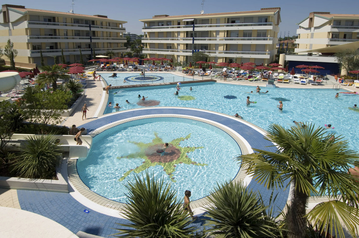 Poolanlage mit Palmen und Menschen vor mehreren mehrstöckigen Gebäuden.