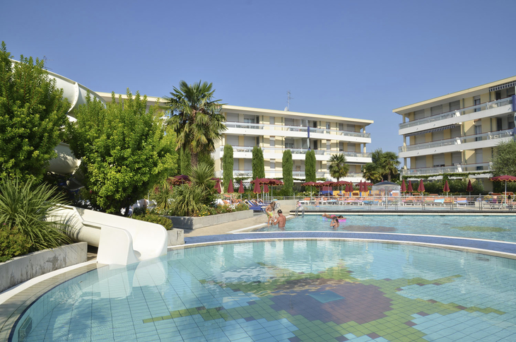 Poolanlage mit Rutschen und Ferienwohnungen im Hintergrund bei sonnigem Wetter