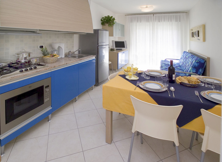 Essbereich mit Tisch, Stühlen, Küche und Sofa in einem Ferienapartment.
