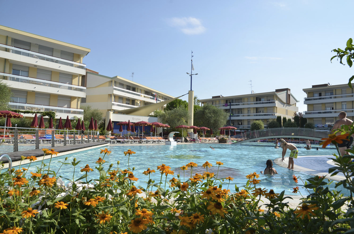 Poolbereich des Villaggio Planetarium Resorts in Bibione mit Gebäuden im Hintergrund.