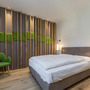 Modern eingerichtetes Schlafzimmer mit grüner Wanddekoration und grüner Stuhl.