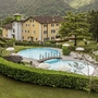 Garten mit Pool und Sonnenschirmen vor einem Hotel, umgeben von Bergen.