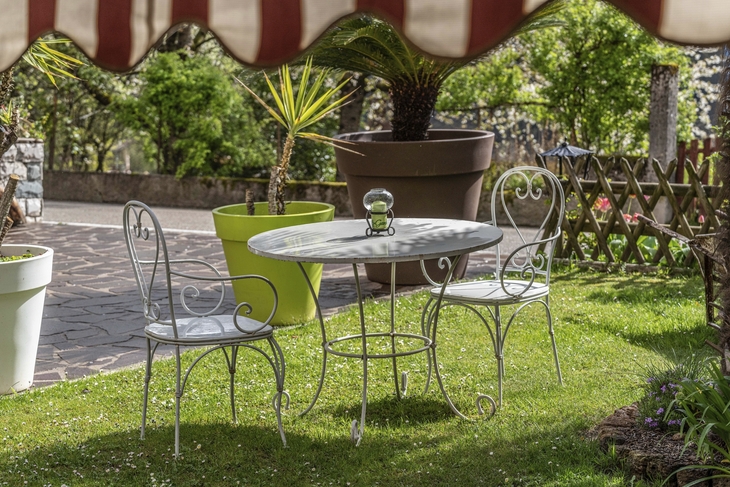 Gartenbereich mit einem Tisch und zwei Eisenstühlen auf einer Wiese.