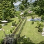 Hotelgarten mit Pool und Liegewiese, umgeben von Bäumen und Hügeln.