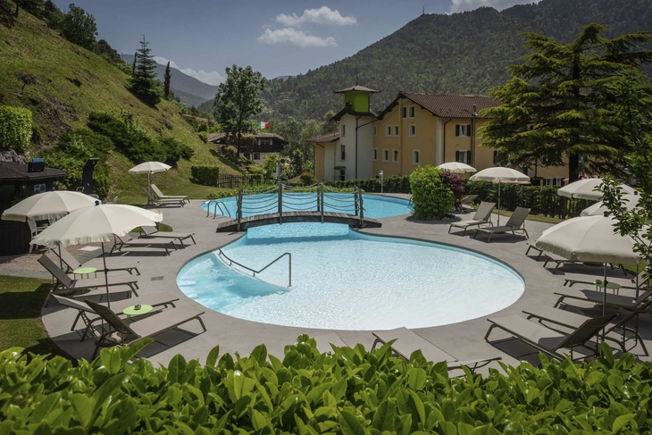 Pool mit Liegestühlen und Sonnenschirmen im Garten eines Hotels in den Bergen.