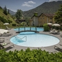 Pool mit Liegestühlen und Sonnenschirmen im Garten eines Hotels in den Bergen.