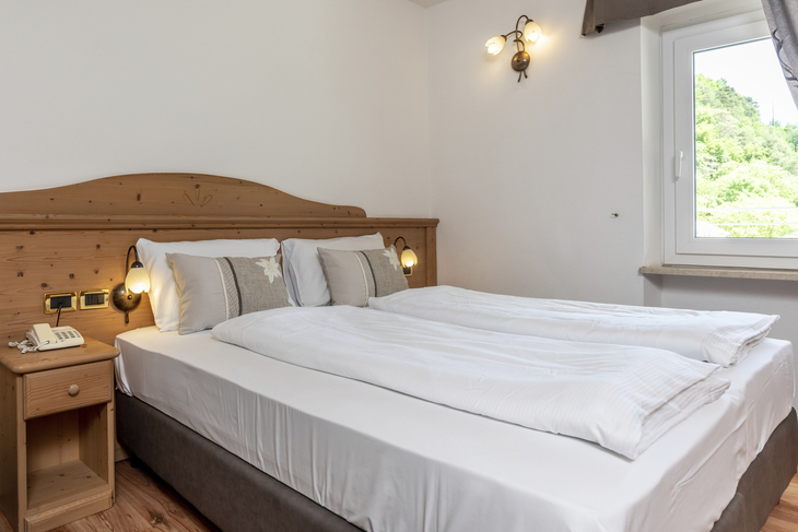 Doppelbett in einem gemütlichen Hotelzimmer mit Holzinterieur und Blick aus dem Fenster.