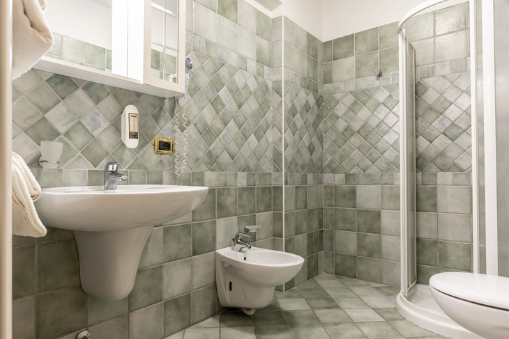 Badezimmer mit grünen Fliesen, Duschkabine, Waschbecken und Bidet.